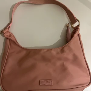 Rosa axelväska från NA-KD - Säljer en söt rosa axelväska från NA-KD med stilren design. Väskan har ett huvudfack med dragkedja och bred axelrem. Perfekt storlek för det viktigaste och enkel att matcha till olika outfits.