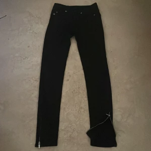 Svarta skinny jeans med dragkedja - Säljer ett par svarta skinny jeans med dragkedja vid benslut och klassisk femficksdesign. Jeansen har låg midja och smal passform, perfekta till sneakers eller boots. Materialet är stretchigt och bekvämt, vilket gör dem lätta att bära hela dagen.