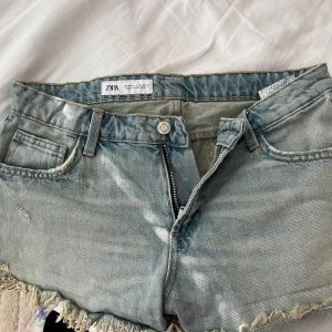 Ljusblå jeansshorts från Zara - Snygga ljusblå jeansshorts från Zara med fransig kant och slitna detaljer. Klassisk femficksmodell med dragkedja och knapp framtill. Perfekta för varma dagar och ger en avslappnad vibe.
