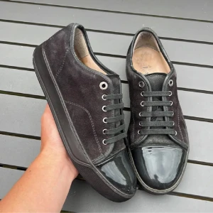 Lanvin skor - Snygga svarta sneakers från Lanvin med ovandel i mjuk mocka och glansig lackad tå. Skorna har rund tå, svarta snören och en platt sula. Perfekt för dig som gillar stilrena och exklusiva detaljer i din vardag.