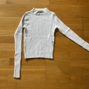 Vit ribbad tröja från Bershka - Säljer en vit ribbad långärmad tröja från Bershka i storlek XS. Tröjan har en högre hals och är figurnära med stretchigt material, perfekt att styla med jeans eller kjol. Enkel och clean look som funkar året runt.