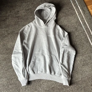 Grå hoodie från Saint Blanc  - Snygg grå hoodie från Saint Blanc i storlek XS. Tröjan har huva, magficka och tryck både fram och bak. Tillverkad i mjuk ekologisk bomull, perfekt för chill dagar. Klassisk passform med ribbade muddar och diskret logga på bröstet.