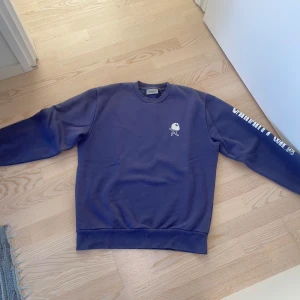Blå/lila sweatshirt från Carhartt WIP - Säljer en blå sweatshirt från Carhartt WIP med vita tryck på bröstet, ryggen och ena ärmen. Tröjan har rund hals, ribbade muddar och en relaxed passform. Perfekt för dig som gillar streetwear och snygga prints.