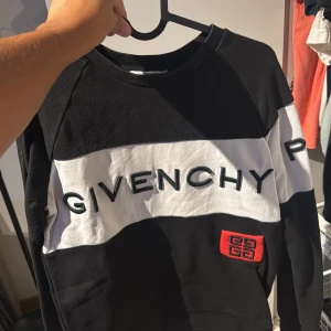 Givenchy Paris svartvit sweatshirt - Säljer en svart och vit sweatshirt från Givenchy Paris med broderad logga över bröstet och röd patch med Givenchy-symbolen. Tröjan har lång ärm och klassisk passform, perfekt för dig som gillar streetstyle och exklusiva märken. Storlek M passar S