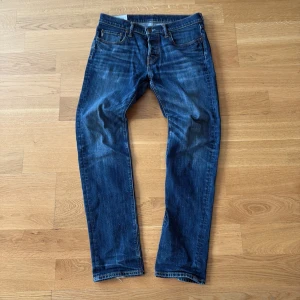 Blå jeans Abercrombie & Fitch 32/32 - Snygga blå jeans från Abercrombie & Fitch i klassisk rak modell. Jeansen har fem fickor, orangea kontrastsömmar och en läderpatch bak i midjan. Tillverkade i slitstarkt denim med en autentisk tvättad look.