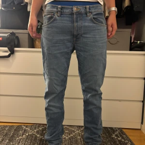 Blå jeans från Nudie Jeans - Säljer ett par klassiska blå jeans från Nudie Jeans med raka ben och snygga kontrastsömmar. Jeansen har fem fickor, normal passform och är tillverkade i mjukt bomullsjeans. Bakfickorna har Nudie Jeans ikoniska broderi.