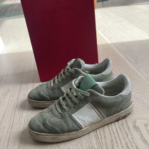 Valentino Garavani sneakers i mocka - Snygga sneakers från Valentino Garavani med box i ljusgrön mocka med vita detaljer och snörning. Skorna har en klassisk låg siluett och en vit platt sula med svart mönstrad undersida. Perfekta för dig som gillar exklusiva och stilrena sneakers.