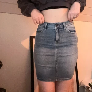 Blå jeanskjol  - Snygg blå jeanskjol från Object i klassisk femficksmodell. Kjolen är kort och har en tight passform med hög midja, bälteshällor och knapp- samt dragkedja framtill. 