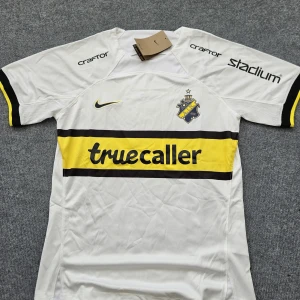 AIK vit matchtröja Nike S - AIK:s vita matchtröja från Nike i Dri-FIT-material. Tröjan har korta ärmar, svart och gul rand över bröstet med truecaller-tryck, AIK-emblem och flera sponsorloggor. Perfekt för dig som vill visa ditt AIK-stöd på läktaren eller i vardagen.