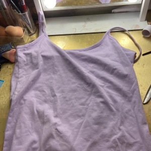 Lavendellila linnetopp från AHLÉNS - Supersöt lavendellila linnetopp från AHLÉNS med tunna axelband. Enkel och stilren design i mjuk bomull, perfekt för varma dagar. Färgen är en ljus lila nyans som verkligen poppar. Snygg att matcha med jeans eller kjol.