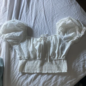 Vit blus med puffärmar och broderi - Superfin vit blus med puffiga kortärmar och broderade detaljer. Toppen har smockad midja, knytning framtill och romantisk känsla. Perfekt för dig som gillar söta och trendiga plagg med volym och spetskänsla.