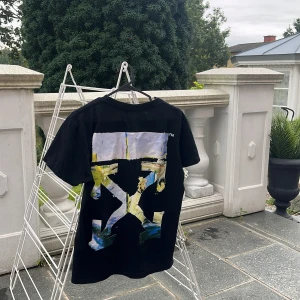 Svart Off-White t-shirt med grafiskt tryck - Svart t-shirt från Off-White med stort grafiskt tryck i färgerna blått, gult och vitt på ryggen. Framtill finns en liten vit Off-White-logga. Riktigt fräsch passar året om, stilig och elegant t-shirt .