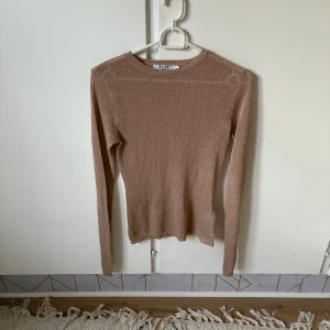 Glittrig beige tröja från NA-KD  - Supersnygg beige långärmad tröja från NA-KD i storlek XS. Tröjan har ett glittrigt material som ger en extra touch och sitter figurnära. Perfekt att styla med jeans eller kjol för en trendig look.