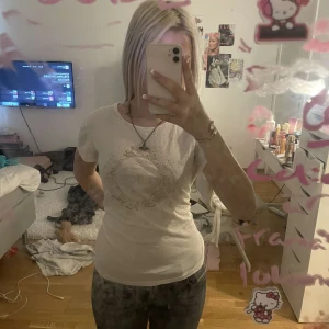 Vit Juicy Couture t-shirt med tryck - Vit t-shirt från Juicy Couture Black Label med ett glittrigt tryck framtill. Klassisk rund halsringning och korta ärmar. T-shirten är i mjuk bomull och har en slim passform som sitter snyggt på kroppen. Perfekt för dig som gillar en clean men ändå glam vibe.