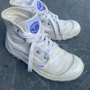 Vita Palladium canvas kängor - Säljer ett par klassiska vita kängor från Palladium i canvas med grov sula och snörning. Skorna har rund tå, tydlig logga på plösen och hälen samt robust känsla. Perfekta för dig som gillar streetstyle och vill ha något som sticker ut. Storlek 37. Pris är diskutabelt;)