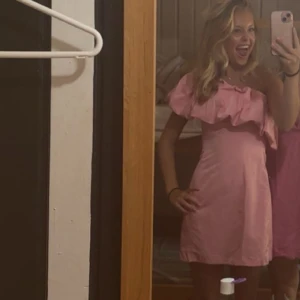 Rosa oneshoulder kortklänning med volang - Säljer en superfin rosa kortklänning med oneshoulder och stor volang upptill. Klänningen har en figurnära passform och är tillverkad i ett mjukt, slätt material som känns skönt mot huden. Som ny, endast använd en gång!