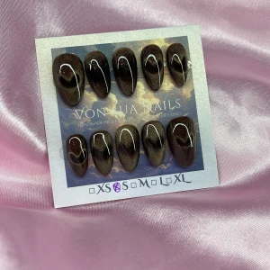 SweetBrown(S);Short Almond;Curved - Snygga handgjorda press-on naglar från Von Sua Nails i en cateye mörkbrun färg med cateyeHjärt-design. Naglarna har en kurvad kort almond-form och kommer i S: 15 mm, 11,5 mm, 12 mm, 11 mm, 9 mm. Perfekt för dig som vill ha en cool och unik look utan att gå till salong.