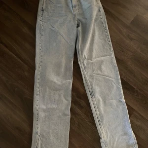 Ljusblå raka jeans med en utsvävning  - Säljer ett par ljusblå jeans med rak passform och klassisk femficksdesign. Jeansen har en enkel look utan slitningar eller detaljer och är tillverkade i denim. Perfekta för dig som gillar en clean och avslappnad stil.