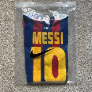 FC Barcelona fotbollströja - Klassisk FC Barcelona fotbollströja med Messi 10 på ryggen. Tröjan är randig i rött och blått med gula detaljer, officiellt klubbmärke på bröstet och Unicef-tryck. Tillverkad i lätt och ventilerande polyester, perfekt för match eller träning. Sponsor märket är lite slitet men inte mycket.