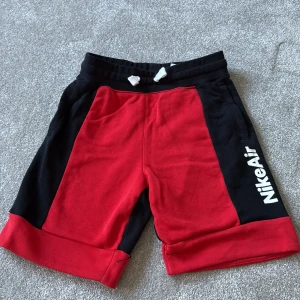 Nike Air röda och svarta shorts M - Nike Air shorts i rött och svart med vit logga på sidan. Mjuk bomullsblandning med elastisk midja och snörning. Snygg kontrast mellan färgerna och breda uppvikta benslut. Perfekta för chill eller sport, klassisk streetstil.