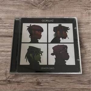 Demon Days - Demon Days av Gorillaz är ett ikoniskt album med coola tecknade karaktärer på omslaget. Perfekt för dig som älskar musik med unik stil och vill ha något som sticker ut i samlingen. Innehåller låtar som 'Feel Good Inc.' och 'DARE'. Skick enligt bilderna. 