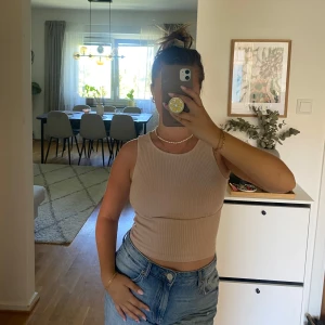 Beige ribbad topp från NA-KD - st S - Supersnygg beige ribbad topp från NA-KD. Modellen är croppad med rund halsringning och ärmlös design. Storlek S. Mjuk och stretchig bomullsblandning som sitter skönt på kroppen.