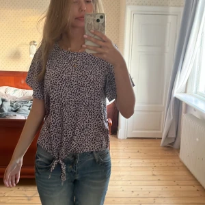 Lila leopardmönstrad blus från Lindex - Säljer en lila blus från Lindex med svart leopardmönster. Toppen har korta ärmar, rund halsringning och en snygg knytning framtill. Perfekt för dig som vill sticka ut lite extra med ett coolt mönster. Storleken är 168/164