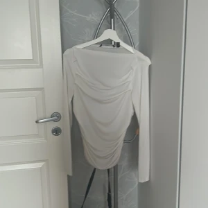 Vit långärmad topp från Vero Moda - Säljer en vit långärmad topp från Vero Moda med snygg drapering framtill. Toppen har en figurnära passform och är tillverkad i ett mjukt, stretchigt material som känns skönt mot huden. Perfekt att styla med jeans eller kjol för en trendig look.