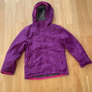 Lila vindjacka från Neomondo - Snygg lila vindjacka från Neo Mondo med huva och rosa detaljer i barnstorlek 140/10 år. Jackan har dragkedja framtill, två fickor med dragkedja och justerbara ärmslut med kardborre. Håller kyla och vind. Fodret är i grått och rosa. Tveka inte att kontakta vid frågor.
