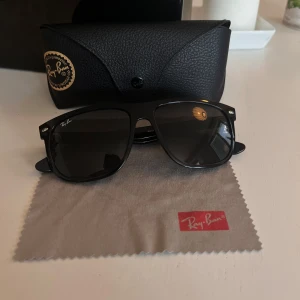 Svarta Ray-Ban boyfriend Solglasögon - Snygga svarta Ray-Ban Boyfriend solglasögon med klassisk fyrkantig form och mörka linser. Bågarna är tillverkade i blank plast och har diskreta silvriga detaljer vid hörnen. Perfekt accessoar för att höja din stil på sommaren.