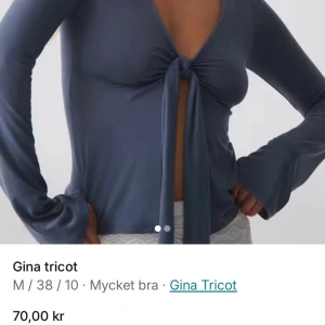 Blå topp med knyt från Gina Tricot - Supersnygg blå topp från Gina Tricot med långa ärmar och knyt framtill som ger en öppen och cool look. Toppens material är mjukt och har en lätt glans. Perfekt för dig som gillar trendiga detaljer och vill sticka ut.