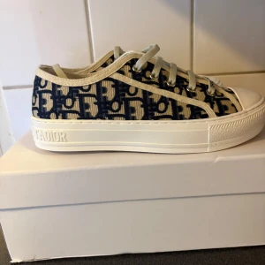 Snearkers med monogram - Snygga sneakers med beige och marinblått monogrammönster. Skorna har vit platt sula, rund tå och snörning med logga på tungan. Tillverkade i canvas med detaljer i syntet. Perfekta för dig som vill sticka ut med lyxig streetstyle.
