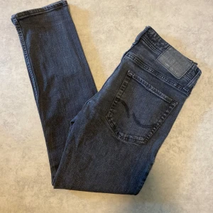 Svarta slimfit/glenn jeans Jack & Jones - Snygga mörkgrå slim fit jeans från Jack & Jones, modell Glenn. Klassisk femficksdesign och smal passform som sitter tajt men ändå bekvämt. Jeansen är tillverkade i ett mjukt denimtyg med lite stretch för extra komfort. 