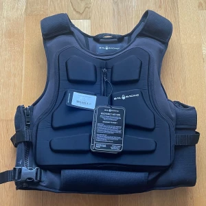 Svart Sail Racing flytväst - Säljer en svart flytväst från Sail Racing med coolt, sportigt utseende och vadderade paneler. Västen har dragkedja framtill, justerbara remmar i sidan och Sail Racing-logga både fram och bak. Perfekt för segling eller andra vattenaktiviteter. Nypris 3000:-