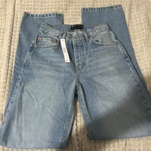 Ljusblåa jeans från ASOS DESIGN - Säljer ett par ljusblåa jeans från ASOS DESIGN med klassisk femficksmodell och knappgylf. Jeansen har raka ben och är tillverkade i bomullsdenim. Perfekta för dig som gillar en avslappnad och tidlös look.