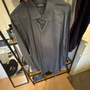 Blå skjorta från Dressmann  - Snygg blå skjorta från Dressmann i premium bomullsstretch. Klassisk krage, långärmad och knäppning framtill. Perfekt för dig som gillar stilrena och enkla plagg med bra passform.