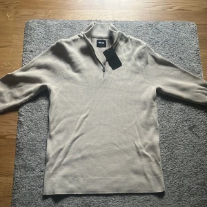 Beige stickad half zip tröja Only & Sons - Snygg beige stickad tröja från Only & Sons med half zip-dragkedja i halsen. Tröjan har långärmad design och ribbade detaljer vid krage och ärmslut. Perfekt för dig som gillar stilren och enkel look med lite edge.