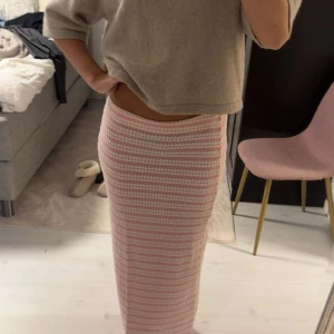 Rosa och vit stickad långkjol - Supersöt långkjol i stickat material med rosa och vita ränder. Kjolen har en tight passform och är perfekt för dig som gillar en trendig look. Mjuk och skön att bära, passar perfekt till en enkel topp eller hoodie.