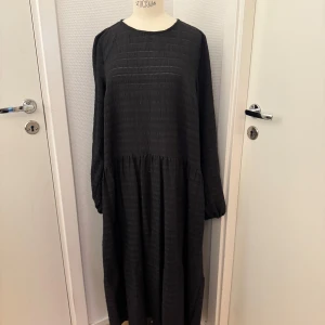 Svart NA-KD långklänning med struktur - NA-KD Svart långklänning med rund hals och långärmade puffärmar. Avslappnad stil. Klänningen har ett strukturerat tyg och ett lätt rynkat midjeparti som ger volym till kjolen. Cool till cowboyboots. Finns på Hägerstensåsen i Stockholm om du vill hämta. 