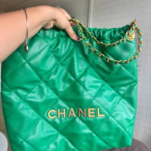 Grön quiltad axelväska  - Säljer en grön quiltad axelväska,med guldfärgade kedjehandtag och läderdetaljer. Väskan har dragskoöppning och klassisk, jag skickar gärna fler bilder . Som ny