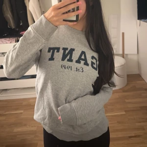 Grå sweatshirt från GANT - Säljer en klassisk grå sweatshirt från GANT med mörkblå logga och text på bröstet. Tröjan har rund halsringning, långa ärmar och ribbade muddar. Perfekt för en chill och stilren look, passar både tjejer och killar.