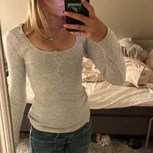 Ljusgrå ribbad långärmad topp H&M XS - Supermjuk och stretchig ljusgrå långärmad topp från H&M i ribbat bomullstyg. Djup rundringning och knappar framtill ger en chill och enkel vibe. Perfekt att styla med jeans eller kjol för en clean look. Elena Gilbert stil