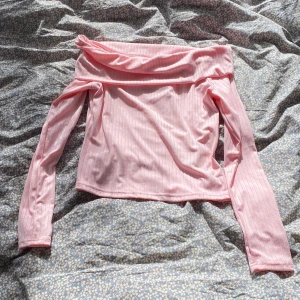 Ljusrosa offshoulder ribbad topp - Säljer en ljusrosa offshoulder topp med långa ärmar. Toppen är ribbad och har en snygg, bred kant upptill som vilar över axlarna. Perfekt för dig som gillar en feminin och trendig stil. Materialet känns mjukt och stretchigt.