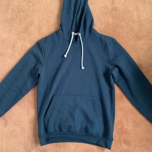 Mörkblå hoodie från Pier One - Säljer en stilren mörkblå hoodie från Pier One med klassisk känguruficka och vita snören i huvan. Tröjan har lång ärm och är tillverkad i mjuk bomull, perfekt för chill dagar eller när du vill ha en enkel look. Köptes för 300 kr 🟥Men jag säljer den för 250🟩