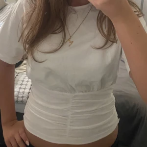 Vit topp - Säljer en vit croppad t-shirt med korta ärmar och snygg snörning i midjan som ger en cool, rynkad effekt. Perfekt för dig som gillar en fräsch och enkel stil med lite edge. T-shirten är gjord i mjuk bomull och sitter riktigt nice på kroppen.