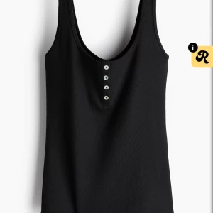 Svart ribbad linnetopp med knappar - Svart ribbad linnetopp med djup rundad hals och fyra små knappar framtill. Perfekt för dig som gillar enkel och stilren design. Materialet är mjukt och stretchigt för en skön passform. Snygg att matcha med jeans eller shorts.