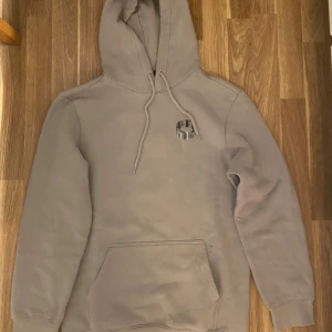 Grå hoodie med tryck Dynamic Vision - Snygg grå hoodie från Dynamic Vision med stor grafisk text på ryggen och mindre tryck på bröstet. Klassisk känguruficka, huva med snörning och mjukt material. Perfekt för dig som gillar streetwear och vill sticka ut lite extra.