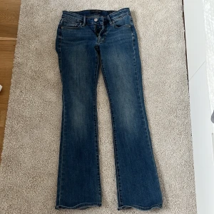 Blå bootcut jeans från Lucky Brand - Snygga blå jeans från Lucky Brand med klassisk bootcut-passform. Jeansen har fem fickor, ljus tvätt och subtila slitningar för en avslappnad look. Tillverkade i mjukt denim med bruna sömmar och läderpatch bak i midjan.
