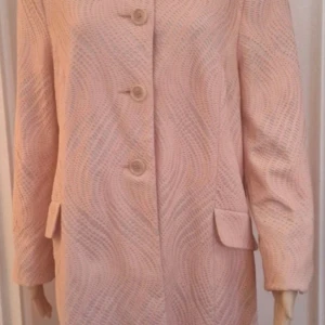 Ljusrosa kappa från Atmosphere - Säljer en laxrosa sommarkappa/trench /lätt kappa i fodrad spets från Atmosphere med snyggt vågigt spetsmönster på foder och knappar framtill. Jackan har klassisk krage, fickor med lock och är helfodrad. Perfekt för dig som vill sticka ut med en unik och feminin stil.1-2ggr på