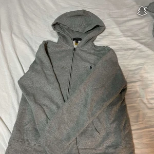 Grå hoodie från Polo Ralph Lauren - Säljer en grå hoodie från Polo Ralph Lauren. Tröjan har huva, dragkedja och fickor framtill. Klassisk Polo-logga broderad på bröstet. Perfekt för chill dagar och enkel att matcha med jeans eller joggers. Passar S. Pris kan diskuteras i snabb affär. 